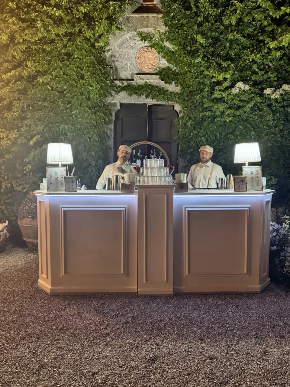 Two bartenders ready behind the lit bar, Castello di Montalto