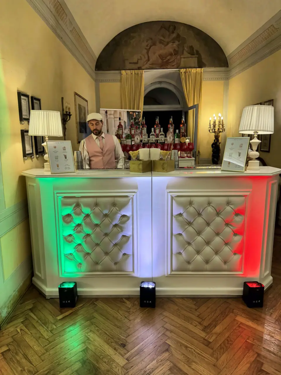 White padded bar lit in Italian colours with bartender, Villa Alta, Pisa