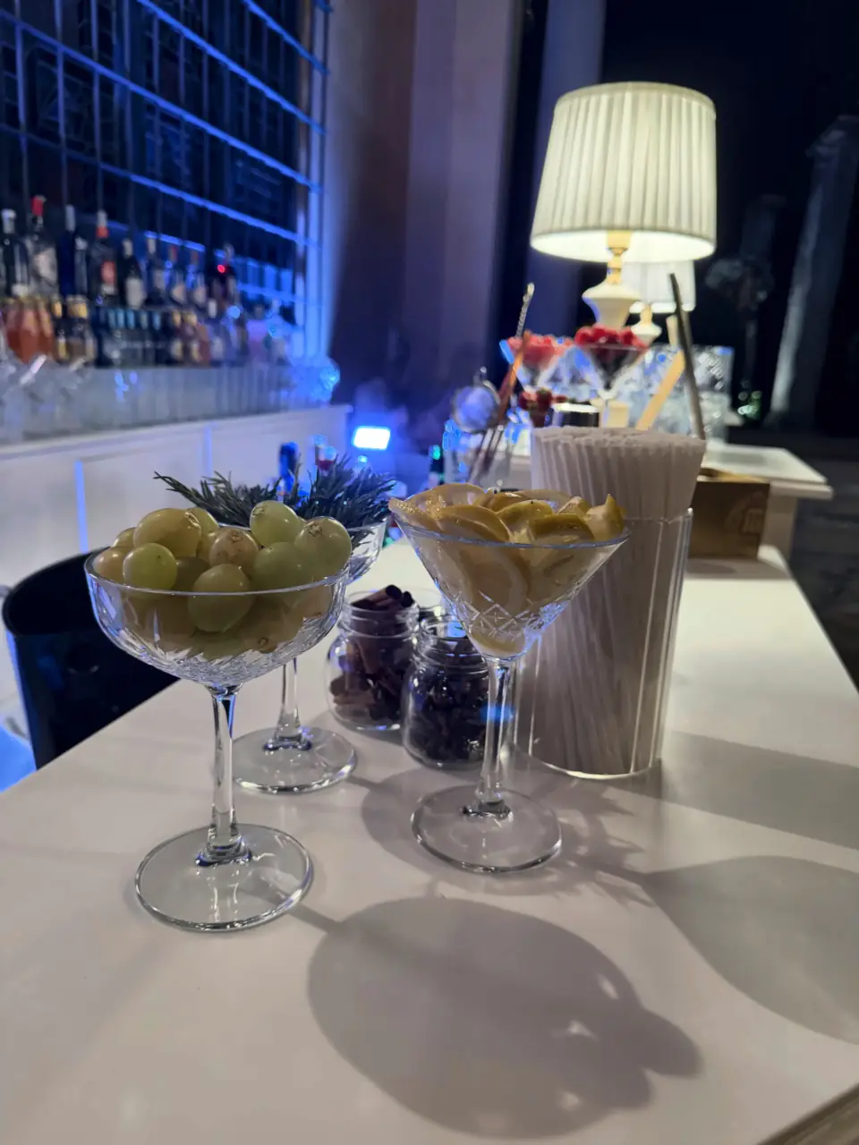 Grapes and lemon in crystal coupes, lit back bar behind
